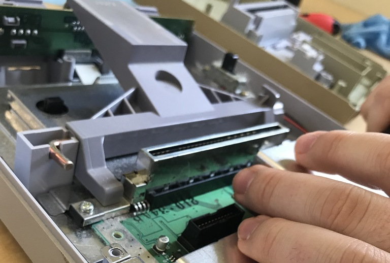 closeup of an open Super Nintendo case, including the main circuit board. A student is using a tool to pry it apart.