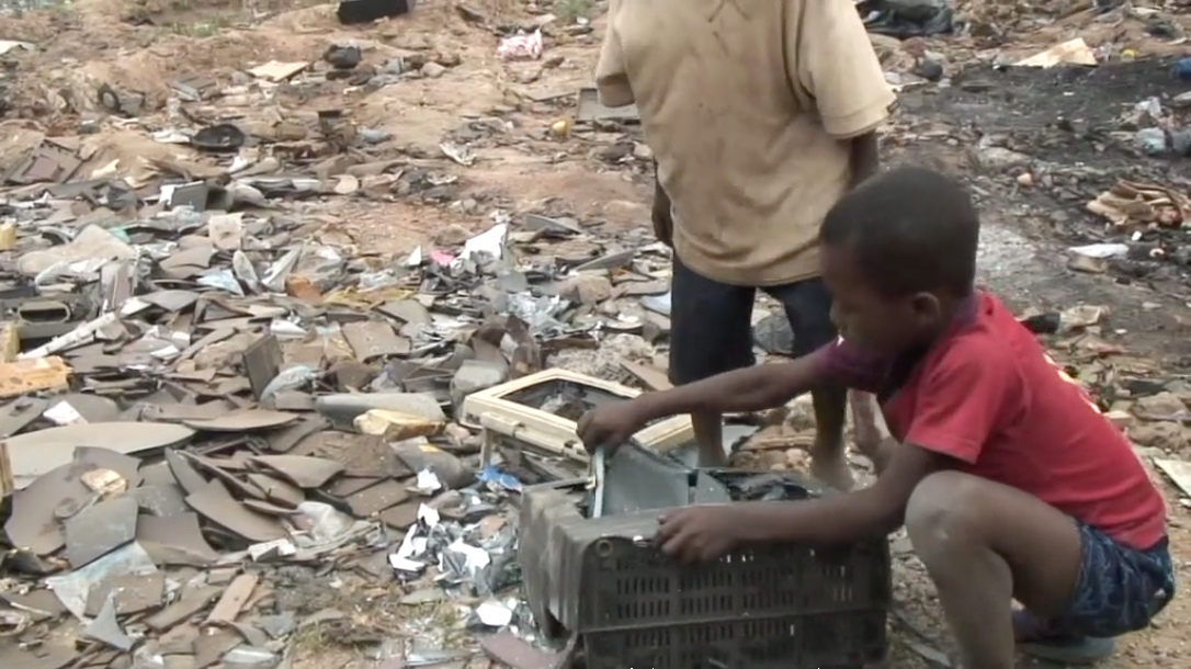 Two children in a junk yard pry the screen off of a television or computer monitor.