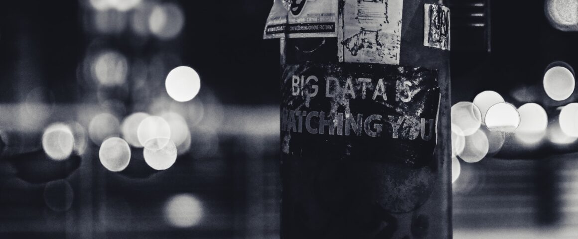 A telephone poll in black and white at night has a poster on it that reads 'Big Data is Watching You.'