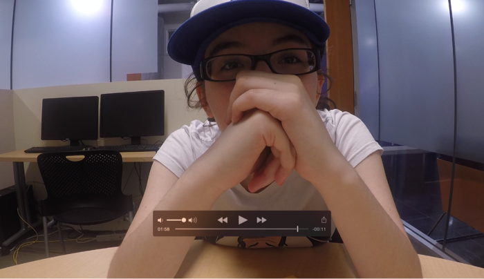 Figure 2: An image of a student sitting in front of a camera with hands clasped together in front of her face.