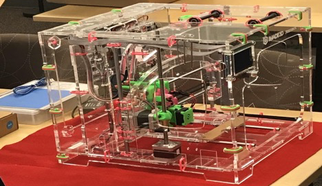 Clear plastic Jellybox 3D printer completely built with pink zip ties and lime green motors.