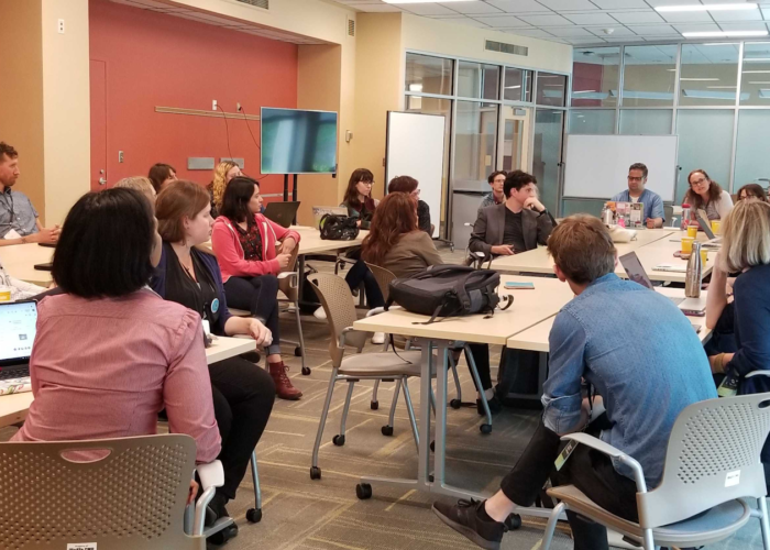 Group of twenty-one symposium attendees sitting in a circle actively engaged in a workshop discussion session.