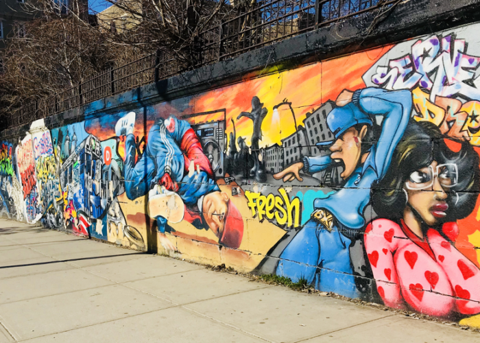 A brightly painted mural located on 166 th Street and Grand Concourse in the Bronx, depicting people in a Bronx cityscape.