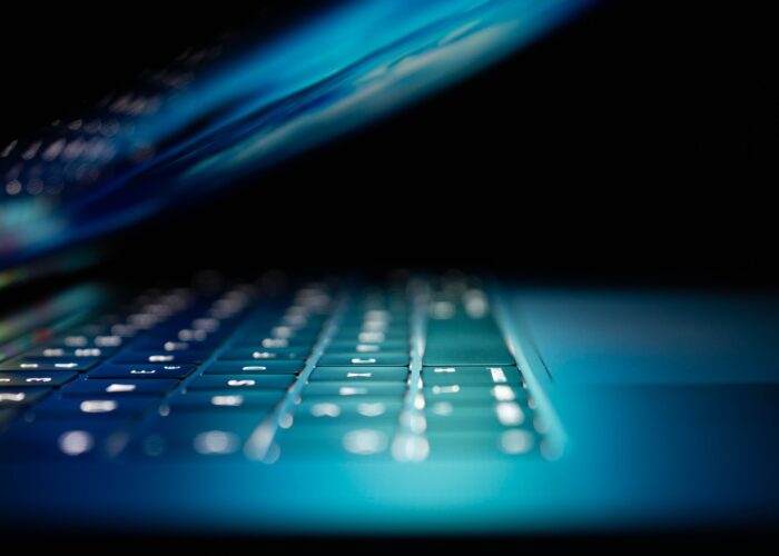 A dimly lit laptop light illuminates a keyboard as it closes.