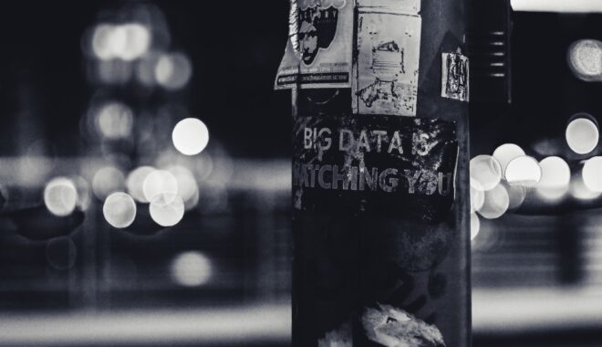 A telephone poll in black and white at night has a poster on it that reads 'Big Data is Watching You.'