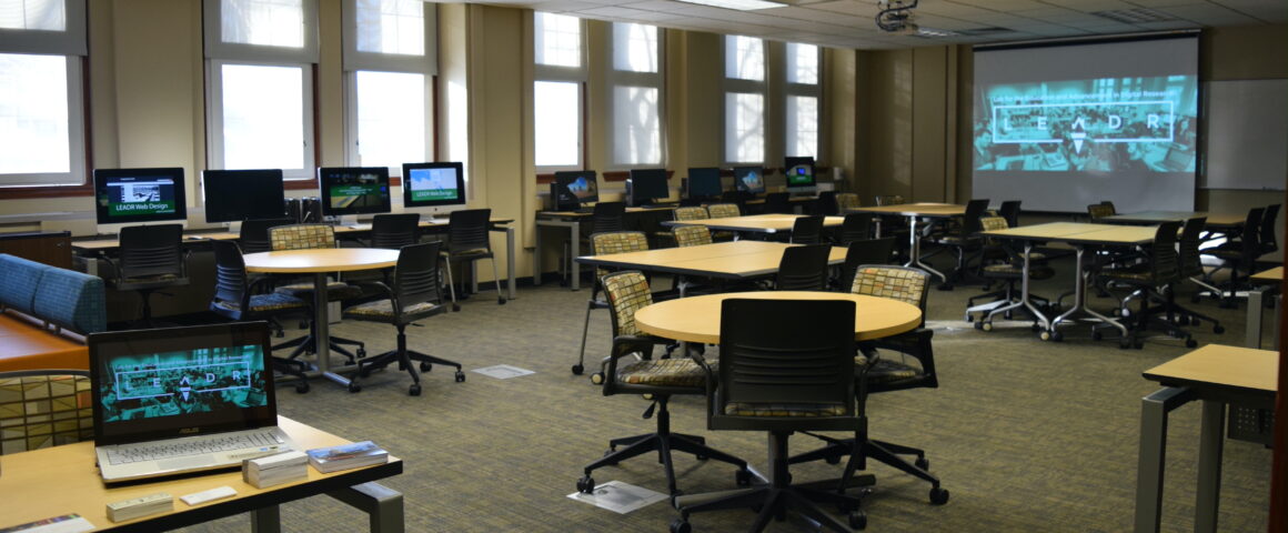 A classroom with many computer monitors reading LEADR sits empty, awaiting students.